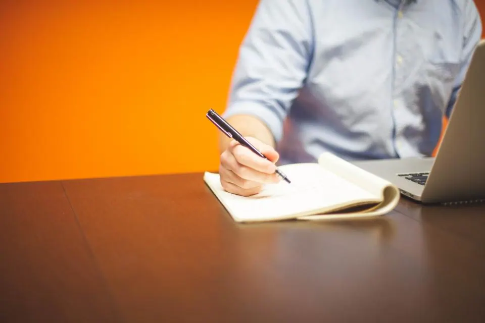 Two people working together at a table with notes, papers and a laptop.